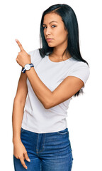 Sticker - Beautiful hispanic woman wearing casual white tshirt pointing with hand finger to the side showing advertisement, serious and calm face