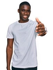 Wall Mural - Young african american man wearing casual white t shirt smiling friendly offering handshake as greeting and welcoming. successful business.