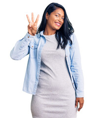 Poster - Hispanic woman with long hair wearing casual denim jacket showing and pointing up with fingers number three while smiling confident and happy.