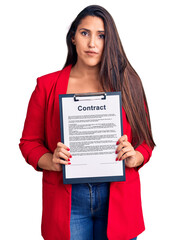 Canvas Print - Young beautiful brunette woman holding clipboard with contract thinking attitude and sober expression looking self confident