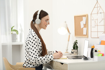 Wall Mural - E-learning. woman taking notes during online lesson at table indoors