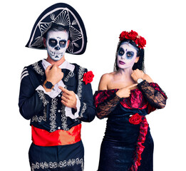 Poster - Young couple wearing mexican day of the dead costume over background in hurry pointing to watch time, impatience, looking at the camera with relaxed expression