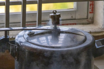 Steam escaping from the pressure cooker's lid with the kitchen's reflection. Pressure cookers are airtight cooking devices that use steam and pressure to cook food quickly. 