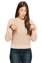 Canvas Print - Young brunette woman wearing casual winter sweater pointing down with fingers showing advertisement, surprised face and open mouth