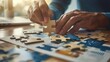 © Moopingz - Close-up of hands placing a puzzle piece on a table with scattered puzzle pieces and charts.