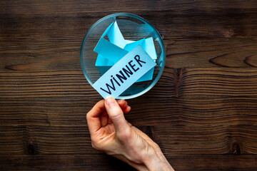 Female hand holding lottery ticket with winner word near glass bowl full of paper sheets. Winner concept