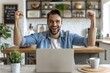 Cheerful young man with stubble looking at laptop screen joyfully raising his hands. Handsome hipster completed successful project, made a lucrative deal. Freelance, creative work and life concept.