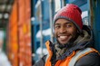 Portrait of male loader wearing orange signal vest working at warehouse. Smiling confident freight handler standing outdoors. Sea containers standing in the background.