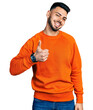 © Krakenimages.com - Young hispanic man with beard wearing casual orange sweater doing happy thumbs up gesture with hand. approving expression looking at the camera showing success.