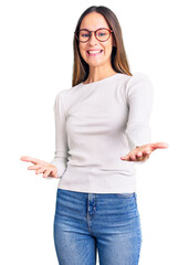 Wall Mural - Beautiful brunette young woman wearing casual white sweater and glasses smiling cheerful with open arms as friendly welcome, positive and confident greetings