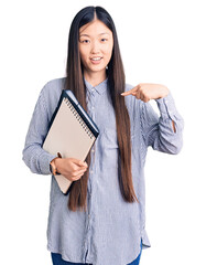 Wall Mural - Young beautiful chinese woman holding notebook pointing finger to one self smiling happy and proud