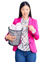 Sticker - Young beautiful chinese woman holding paper bin full of crumpled papers smiling happy pointing with hand and finger