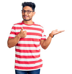 Wall Mural - Handsome latin american young man wearing casual clothes and glasses showing palm hand and doing ok gesture with thumbs up, smiling happy and cheerful