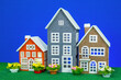 Three toy houses of different sizes with flowers nearby on a blue background