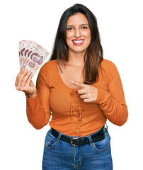 Sticker - Beautiful hispanic woman holding mexican pesos smiling happy pointing with hand and finger