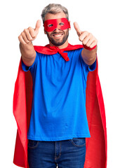 Poster - Young blond man wearing super hero custome approving doing positive gesture with hand, thumbs up smiling and happy for success. winner gesture.