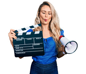 Canvas Print - Young blonde woman holding video film clapboard and megaphone making fish face with mouth and squinting eyes, crazy and comical.