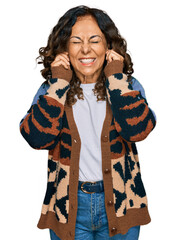 Canvas Print - Middle age hispanic woman wearing casual clothes covering ears with fingers with annoyed expression for the noise of loud music. deaf concept.