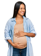 Poster - Beautiful hispanic woman expecting a baby showing pregnant belly looking away to side with smile on face, natural expression. laughing confident.