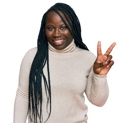 Wall Mural - Young black woman with braids wearing casual winter sweater smiling with happy face winking at the camera doing victory sign. number two.