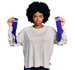 Poster - Young african american woman holding socks skeptic and nervous, frowning upset because of problem. negative person.