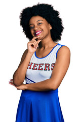 Wall Mural - Young african american woman wearing cheerleader uniform looking confident at the camera with smile with crossed arms and hand raised on chin. thinking positive.