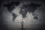 Fototapeta Kosmos - Person stands in front of a concrete wall looking at the world map. Travel limitations concept