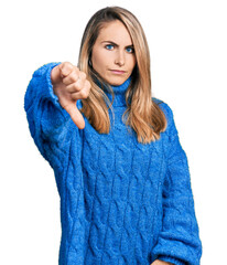 Wall Mural - Young blonde woman wearing casual sweater looking unhappy and angry showing rejection and negative with thumbs down gesture. bad expression.