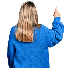 Wall Mural - Young blonde woman wearing casual sweater posing backwards pointing ahead with finger hand