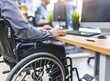 Disabled person in the wheelchair works in the office at the computer. He is smiling and passionate about the workflow.