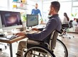 © Svetlana - Disabled person in the wheelchair works in the office at the computer. He is smiling and passionate about the workflow.