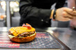 © pavel siamionov - Freshly prepared cheeseburger with bacon on a star-patterned surface in a bustling kitchen, highlighting the appeal of fast food