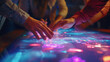 A group of people are touching a glowing table with their hands. The table is illuminated with neon colors and the people are focused on it