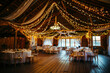 The picture shows a rustic barn reception area adorned with draping white fabric and warm fairy lights, creating an enchanting and romantic atmosphere.