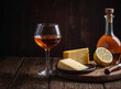 Close-up of a glass of cognac and a bottle of cognac on a wooden table near a wooden wall. The character and all objects are fictitious, the image was created using the neural network Fooocus v2