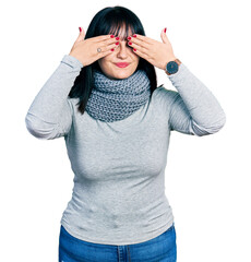 Poster - Young hispanic plus size woman wearing winter scarf covering eyes with hands smiling cheerful and funny. blind concept.