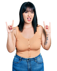 Sticker - Young hispanic plus size woman wearing casual clothes shouting with crazy expression doing rock symbol with hands up. music star. heavy concept.