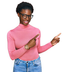 Wall Mural - Young african american girl wearing casual clothes and glasses smiling and looking at the camera pointing with two hands and fingers to the side.