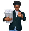 Young african american girl holding paper bin full of crumpled papers annoyed and frustrated shouting with anger, yelling crazy with anger and hand raised