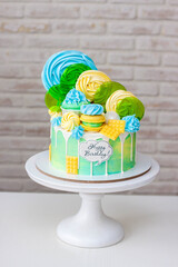 Wall Mural - Colorful green and yellow beautiful birthday cake on white background with lollipops and meringues on the top