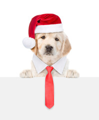 Wall Mural - Golden retriever puppy wearing necktie and santa hat looks above empty white banner. isolated on white background