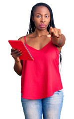 Wall Mural - Young african american woman holding touchpad pointing with finger to the camera and to you, confident gesture looking serious