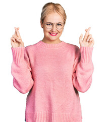 Wall Mural - Young blonde woman wearing casual clothes and glasses gesturing finger crossed smiling with hope and eyes closed. luck and superstitious concept.