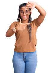 Wall Mural - Young african american woman with braids wearing casual clothes and glasses smiling making frame with hands and fingers with happy face. creativity and photography concept.