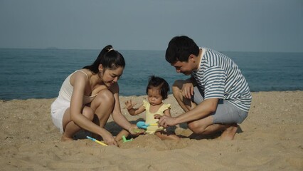 Wall Mural - toddler baby girl playing sand toy with her father and mother. happy family on the sea beach