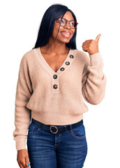 Poster - Young african american woman wearing casual clothes smiling with happy face looking and pointing to the side with thumb up.