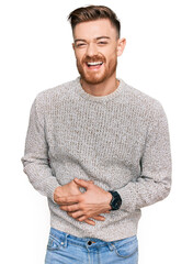 Wall Mural - Young redhead man wearing casual winter sweater smiling and laughing hard out loud because funny crazy joke with hands on body.