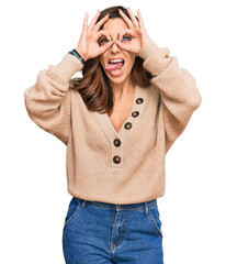 Wall Mural - Young brunette woman wearing casual winter sweater doing ok gesture like binoculars sticking tongue out, eyes looking through fingers. crazy expression.