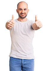 Wall Mural - Young handsome man wearing casual t shirt approving doing positive gesture with hand, thumbs up smiling and happy for success. winner gesture.