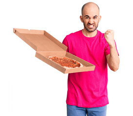 Canvas Print - Young handsome man holding delivery pizza cardboard box annoyed and frustrated shouting with anger, yelling crazy with anger and hand raised